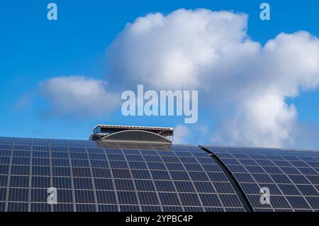 Les panneaux solaires incurvés installés sur un toit génèrent de l’énergie propre sous un ciel bleu nuageux, mettant en valeur des pratiques énergétiques durables Banque D'Images