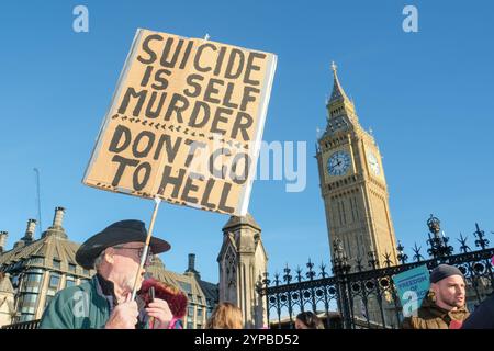 Londres, Royaume-Uni. 29 novembre 2024. Un chrétien opposé à l'aide à mourir se tient devant le Parlement lors d'un débat parlementaire et les députés votent en deuxième lecture sur le projet de loi sur l'aide à mourir avec une pancarte disant: "Le suicide est l'auto-assassinat. Ne va pas en enfer. » Crédit : onzième heure photographie/Alamy Live News Banque D'Images