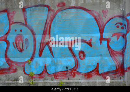 A lettres bleues et grises et épaisses lignes rouges et cerises avec bordures rouges. Un graffiti représentant le mot KOWAH est sur une clôture en béton grise et brune. Banque D'Images