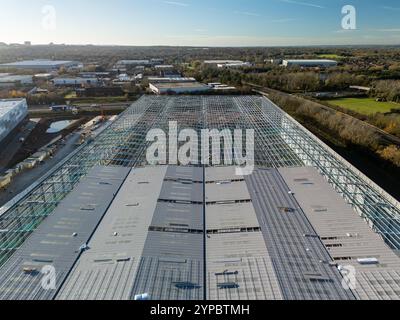 Vue aérienne d'un grand bâtiment industriel en construction, présentant une toiture métallique et une ossature exposée sur fond de banlieue Banque D'Images