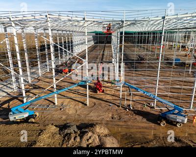 Les ouvriers de la construction utilisent des plates-formes de levage pour construire le cadre en acier d'un grand entrepôt industriel Banque D'Images