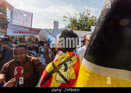 Un homme vêtu d'un drapeau mozambicain s'adresse à la foule avec un mégaphone lors d'une manifestation, tandis que les participants tiennent des banderoles pour soutenir une cause Banque D'Images