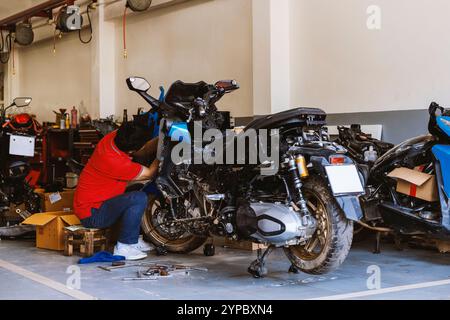 mécanicien qualifié réparant une moto dans un atelier, entouré d'outils et de pièces de rechange, capturant l'essence du travail d'entretien et de réparation Banque D'Images