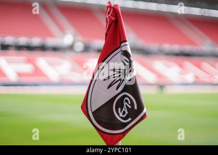 Symbolbild für den SC Freiburg, Eckfahne mit Vereinslogo im Fokus, schwarz-Weiß-rotes Design mit dem stilisierten Greif, unscharfer Hintergrund zeigt Stadiontribünen und Spielfeld, sonnige Beleuchtung betont die Farben, Identität Heimat, repräsentiert und Vereinsstolz, dynamische Perspektive vermittelt Nähe zum Spielgeschehen für Fußballkultur repr Banque D'Images