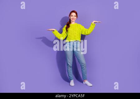 Jeune femme brillante en tricot vert faisant des gestes de promotion sur fond violet. Banque D'Images