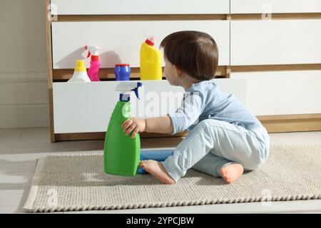 Petit garçon jouant avec des bouteilles de détergents près de l'armoire à la maison. Enfant en danger Banque D'Images