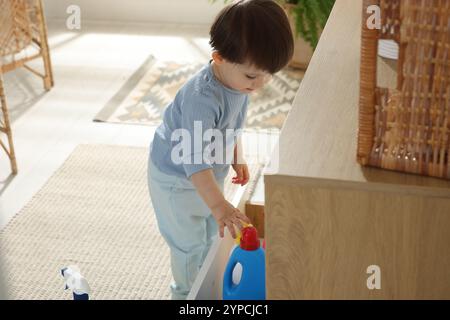 Petit garçon jouant avec des bouteilles de détergents près de l'armoire à la maison. Enfant en danger Banque D'Images