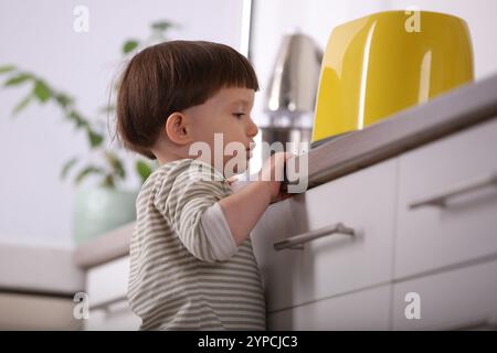 Petit garçon jouant avec le grille-pain dans la cuisine. Situation dangereuse Banque D'Images