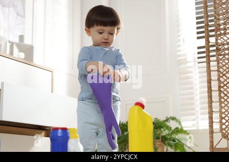 Petit garçon jouant avec un gant parmi les bouteilles de détergents près de l'armoire à la maison. Enfant en danger Banque D'Images