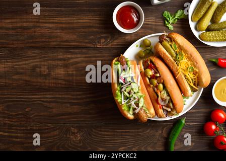 Hot-dogs chargés de garnitures assorties sur fond en bois avec espace libre. Vue de dessus, pose à plat Banque D'Images