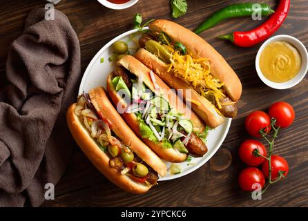 Hot-dogs avec différentes garnitures sur plaque blanche sur fond en bois. Vue de dessus, pose à plat Banque D'Images