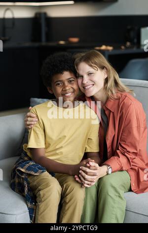 Portrait de mère embrassant son fils tout en étant assise sur un canapé dans un salon moderne, montrant à la fois le bonheur et le confort tout en regardant la caméra et en souriant Banque D'Images