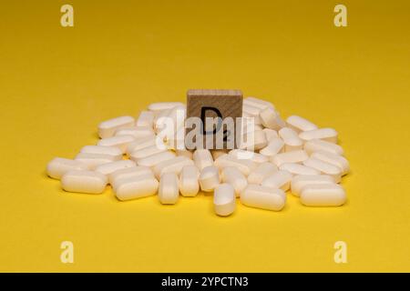 Concept de 'vitamine d' avec pile de comprimés et lettre en bois sur la surface jaune Banque D'Images