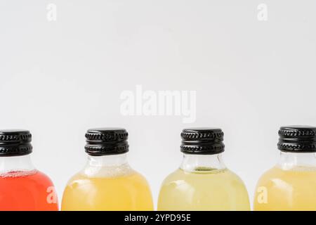 Gros plan de petites bouteilles en verre transparent avec des bouchons noirs, remplis de kombucha de jaune, vert et rouge sur une surface blanche. Vue de face. Copier l'espace Banque D'Images