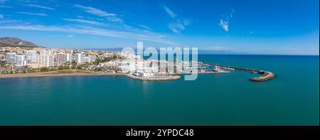 L'image capture une vue aérienne de Benalmadena, en Espagne, avec une marina avec des bateaux, des plages de sable, des gratte-ciel, une grande roue et des montagneuses Banque D'Images