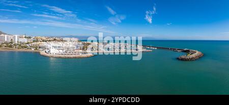 Vue aérienne de Benalmadena, Espagne, avec un port de plaisance avec des bateaux, une grande roue, des bâtiments blancs modernes, et la mer Méditerranée avec un mont lointain Banque D'Images