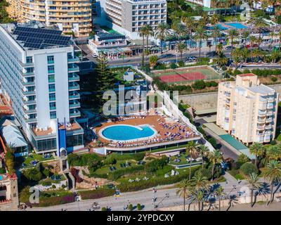 Vue aérienne d'un complexe de Benalmadena en Espagne avec une grande piscine, des panneaux solaires sur le toit de l'hôtel, des courts de tennis et des jardins luxuriants avec des palmiers. Banque D'Images