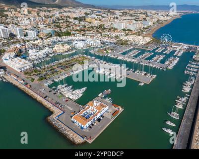 L'image capture une vue aérienne de Benalmadena, en Espagne, avec une marina animée avec des yachts, une grande roue et un mélange de moderne et traditionnel A. Banque D'Images