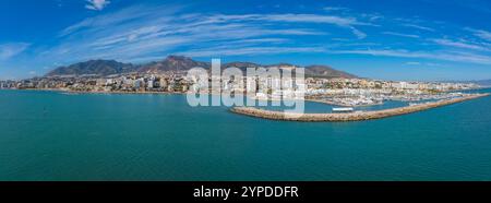 Vue aérienne de Benalmadena, Espagne, avec une marina avec des bateaux, des bâtiments blancs et pastel, et des montagnes en arrière-plan sous un ciel bleu clair. Banque D'Images