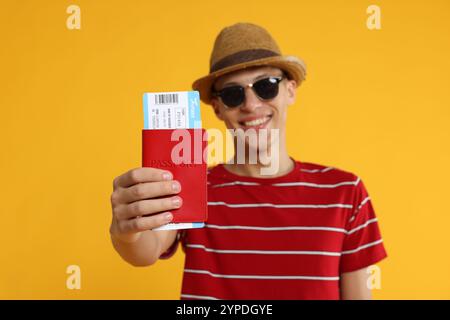 Voyageur heureux dans des lunettes de soleil avec passeport et billet sur fond jaune, focus sélectif Banque D'Images