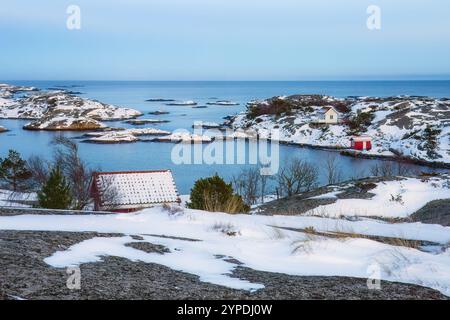 Cabanes côtières avec toits enneigés, terrain glacé et mer bleue calme. Scène pittoresque avec des maisons et un paysage gelé, idéal pour backgrou d'hiver Banque D'Images