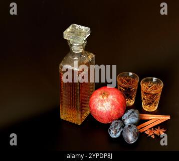 Liqueur de prune-grenade à la cannelle et à l'anis sur fond noir, alcool maison dans un bol en cristal avec épices. Gros plan. Banque D'Images