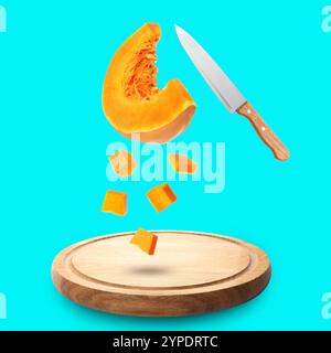 Morceaux de citrouille crue fraîche et couteau dans l'air sur planche de bois sur fond turquoise Banque D'Images