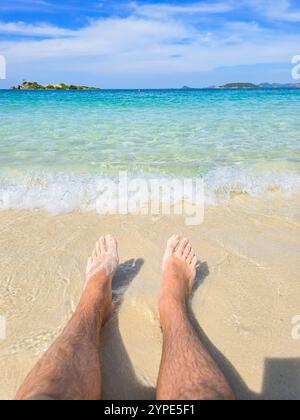 Les eaux cristallines baignent doucement la plage de sable de Samae San Island tandis que la lumière chaude du soleil baigne la scène tranquille. Les pieds s'enfoncent légèrement dans le sable mou, capturant un moment de sérénité. Banque D'Images