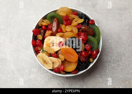 Mélange de différents fruits secs dans un bol sur une table texturée grise, vue de dessus Banque D'Images