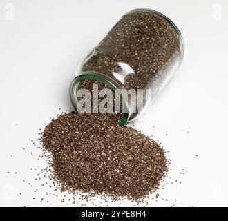 Graines de chia coulant d'un récipient en verre. Banque D'Images