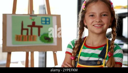Portrait d'écolière mignonne debout avec les bras croisés à table dans la classe de dessin 4k Banque D'Images
