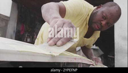 Vue de face d'un batteur de panneaux mâle africain dans un atelier de township, peinture carrosserie d'une voiture, moti lent Banque D'Images