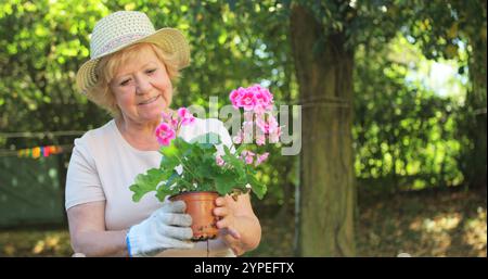 Femme senior examinant la plante en pot dans le jardin par une journée ensoleillée Banque D'Images