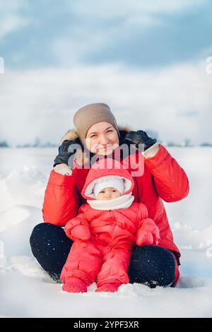 Heureuse mère et bébé sont assis sur la neige et profitent d'une belle journée d'hiver Banque D'Images