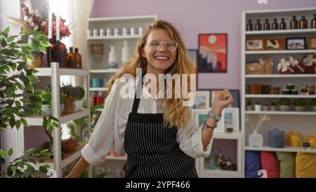 Femme blonde souriante dans un magasin de décoration, portant des lunettes et un tablier, entourée de divers objets décoratifs, plantes et étagères, créant un inv Banque D'Images