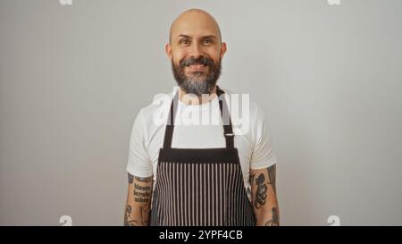 Bel homme hispanique avec une barbe et des tatouages portant un tablier souriant avec confiance sur un fond blanc isolé Banque D'Images