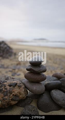 Pierres empilées sur la plage de famara, lanzarote, îles canaries pendant la lumière du jour mettant en valeur calme, paysage extérieur avec des éléments rocheux et un bord de mer serein Banque D'Images