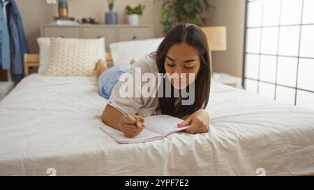 Jeune femme brune se trouve sur un lit dans une chambre confortable écrivant dans un cahier entouré d'un décor serein à la maison Banque D'Images