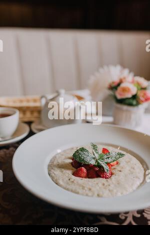 Un petit-déjeuner de café confortable avec un bol de flocons d'avoine crémeux garni de baies fraîches, associé à une tasse de thé à la vapeur Banque D'Images