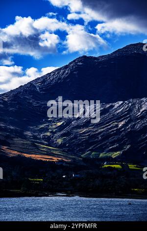 Un ciel bleu vif avec des nuages blancs moelleux. Il y a deux grandes collines couvertes d'herbe et de formations rocheuses. Une fine ligne d'arbres verts et un petit bui Banque D'Images