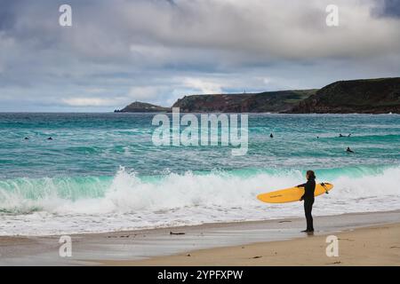 Surfeurs dans la mer à Sennen Cove un jour d'automne avec la côte en arrière-plan Cornwall Angleterre Royaume-Uni Banque D'Images