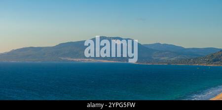 L'image capture une vue aérienne de Tarifa, en Espagne, avec la mer bleue, la chaîne de montagnes lointaine, et les kite surfeurs avec des cerfs-volants colorés le long du sho Banque D'Images