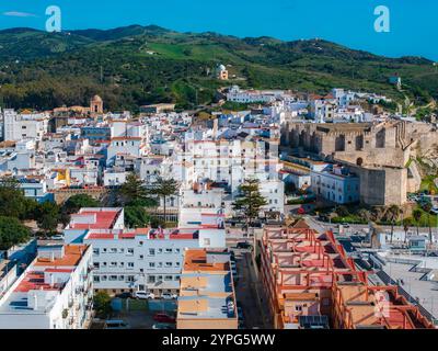 L'image capture une vue aérienne de Tarifa, en Espagne, avec le château de Guzman sur la droite, des bâtiments blanchis à la chaux, des rues étroites et des collines verdoyantes. Banque D'Images