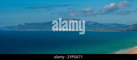 L'image capture une vue aérienne de Tarifa, en Espagne, avec un océan bleu, une plage de sable et un paysage montagneux sous un ciel clair avec cl dispersé Banque D'Images