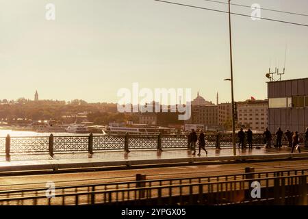 Istanbul, TR - 23 octobre 2024 les personnes traversant le pont de Galata sont silhouettées contre la lumière dorée du jour. Le pont déborde d'activité Banque D'Images