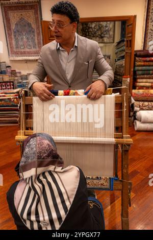 Istanbul, TR - Oct 23, 2024 Une femme démontre le tissage de tapis turc au métier à tisser, fabriquant des motifs complexes, tandis que le propriétaire explique le traditi Banque D'Images