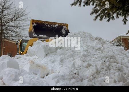 La machinerie lourde enlève activement des tas de neige massifs de la rue résidentielle du parc de stationnement le jour neigeux. Banque D'Images