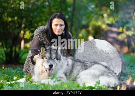 Portrait d'une chamane avec un chien Malamute d'Alaska à côté du feu dans la forêt Banque D'Images