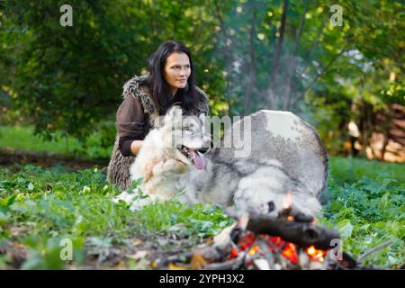 Femme chamane avec un chien Malamute d'Alaska à côté du feu dans la forêt Banque D'Images