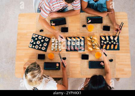 Groupe multiethnique de jeunes amis se réunissant à la maison et mangeant des sushis - personnes heureuses multiraciales se liant tout en déjeunant Banque D'Images